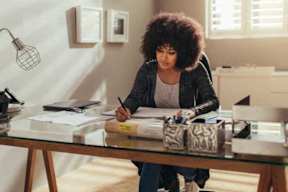 A woman is sitting at a desk writing on a piece of paper.