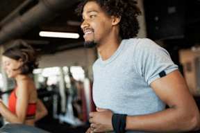 A man with curly hair is running on a treadmill in a gym.