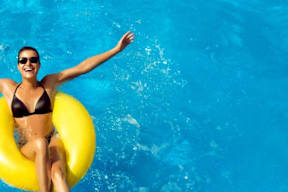 A woman in a black bikini is floating on a yellow inflatable ring in a blue pool.