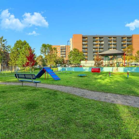 A playground with a blue slide and a red slide in front of a building.