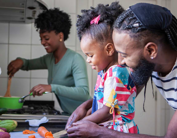 A man and a little girl are cutting vegetables on a cutting board.