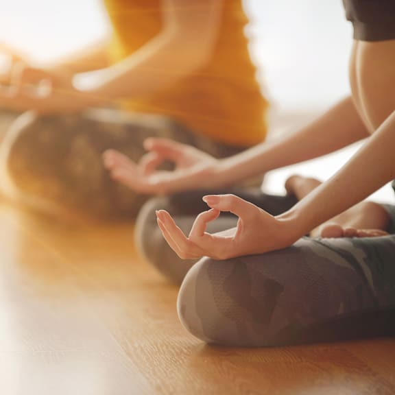 A group of people are sitting cross-legged on the floor in a yoga class.