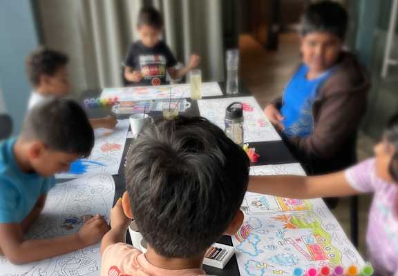 A group of children are sitting at a table coloring.