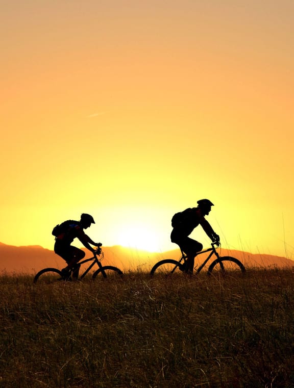 people riding bikes on a hill at sunset