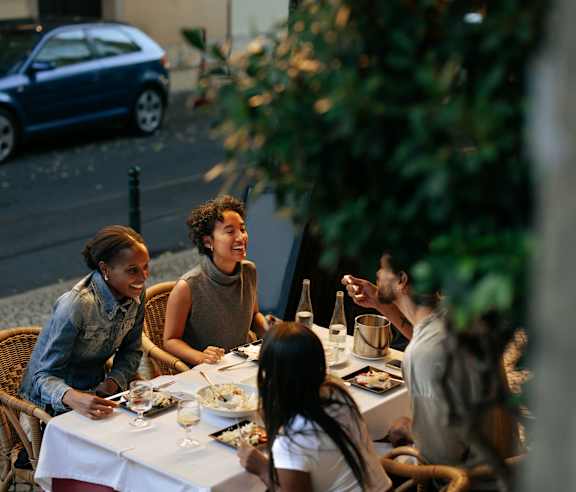 A group of people are sitting at a table outside, enjoying a meal together.