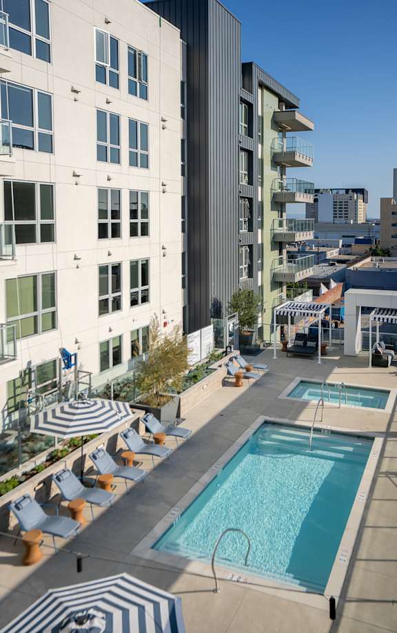 A swimming pool with lounge chairs and umbrellas on a rooftop.
