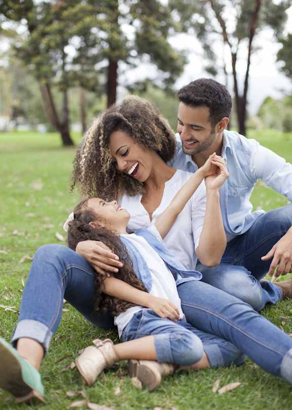 A family of three is sitting on the grass in a park.