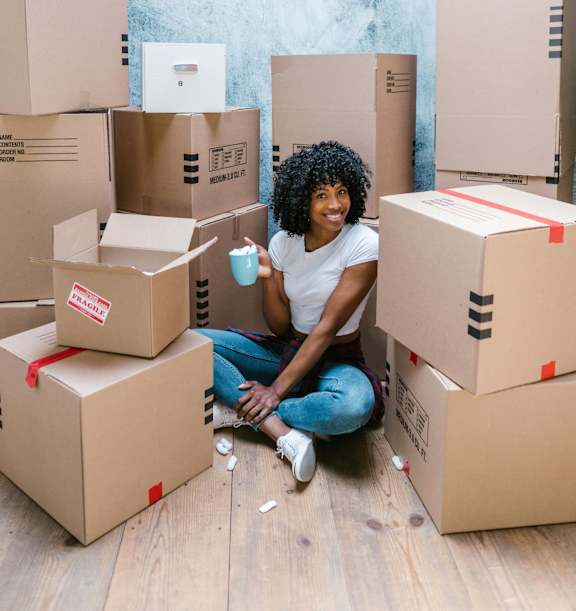 A person is sitting on the floor surrounded by cardboard boxes.