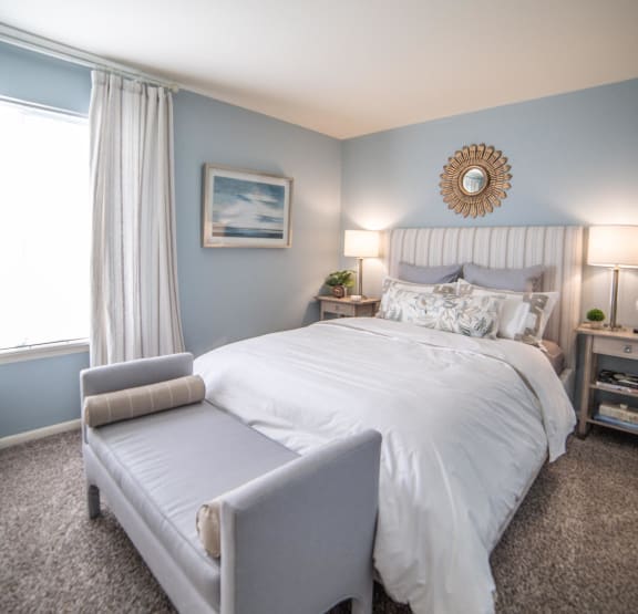 a bedroom with a white bed and blue walls and a window  at Scarborough Lake Apartments in Indianapolis, IN