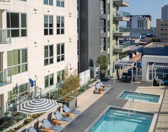 A swimming pool with lounge chairs and umbrellas on a rooftop.