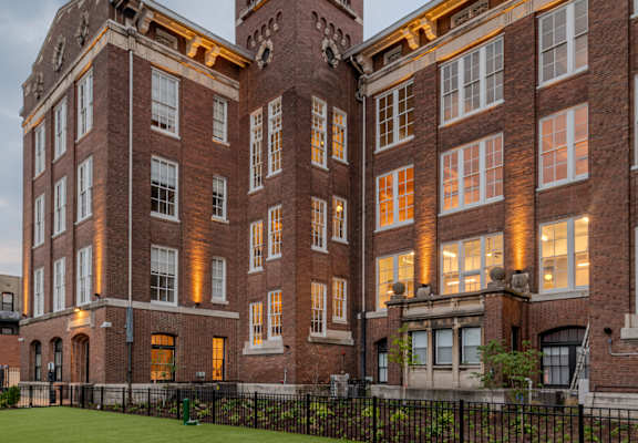 a large brick building with a green lawn and a fence