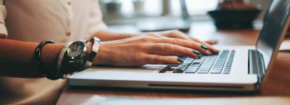 A person is typing on a laptop with a watch on their wrist.