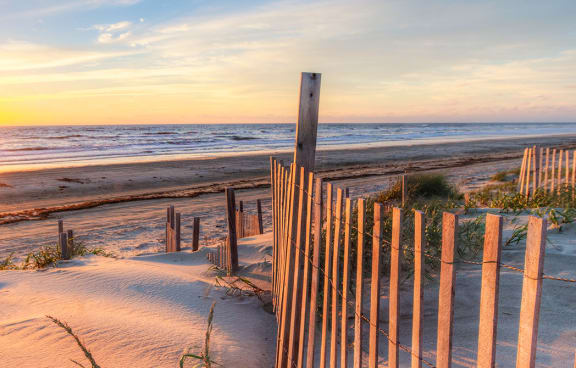 a sunset over a beach with a wooden fence in the foreground