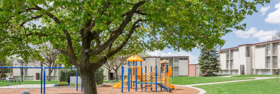 a playground with a tree in the foreground and a building in the background