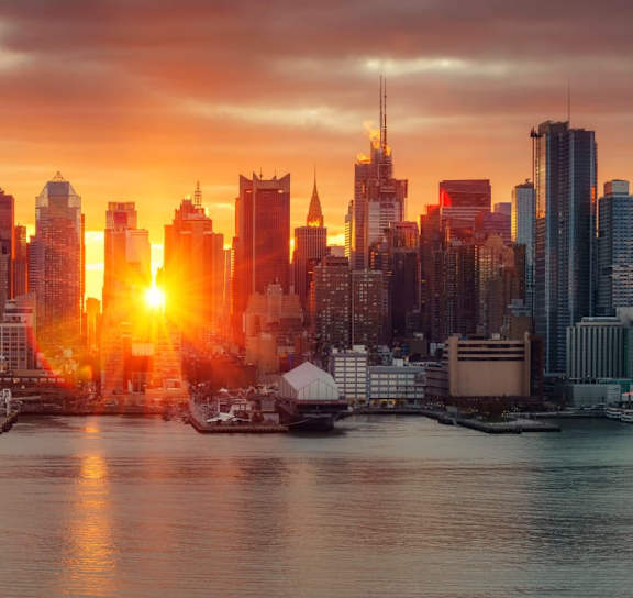 A city skyline at sunset with the sun setting behind the buildings.at 21 West, New York, 10006