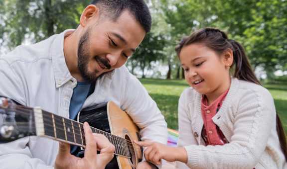 a man and a girl playing a guitar in the park