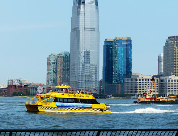 A yellow boat with people on it is in the foreground of a city skyline.