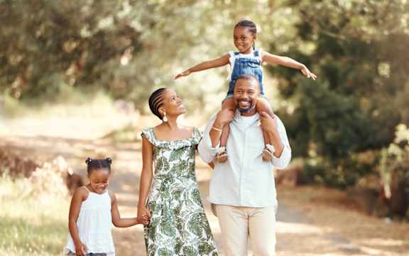 A family of four is walking down a dirt road holding hands.