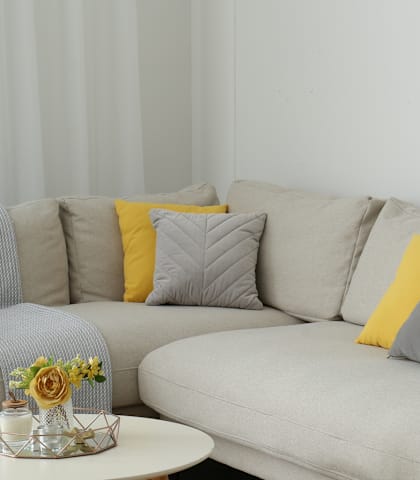 A grey couch with a yellow pillow and a small table with flowers on it.