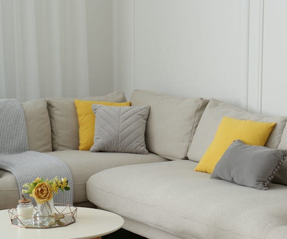 A grey couch with a yellow pillow and a small table with flowers on it.