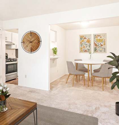 A living room with a grey couch, a wooden coffee table, and a large clock on the wall at West Wind Apartments, Fort Wayne, IN