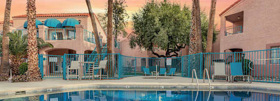 A pool surrounded by palm trees and a building with blue awnings.