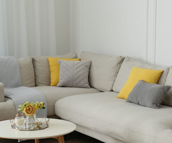 A grey couch with a yellow pillow and a small table with flowers on it.