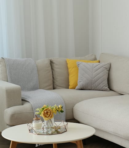 A grey couch with a yellow pillow and a small table with flowers on it.