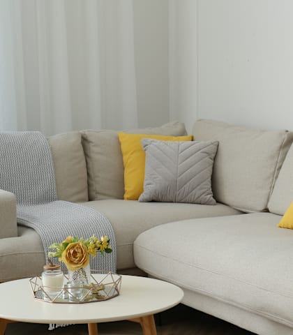 A grey couch with a yellow pillow and a small table with flowers on it.