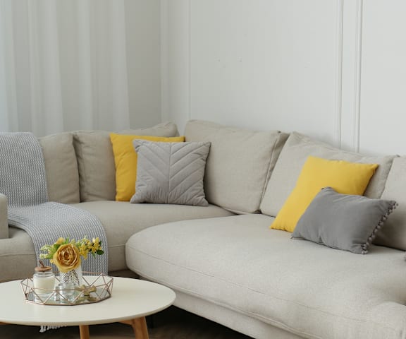 A grey couch with a yellow pillow and a small table with flowers on it.