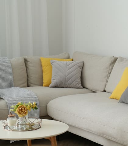 A grey couch with a yellow pillow and a small table with flowers on it.