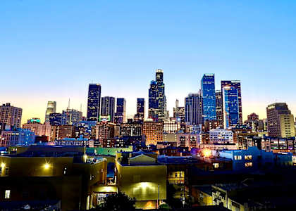 A city skyline at dusk with buildings illuminated against a darkening sky.