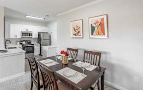 A dining room with a table set for two and a kitchen in the background.