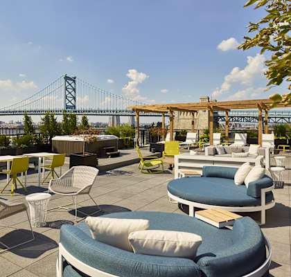 a rendering of a rooftop patio with chairs and tables with a bridge in the background at 11 Cooper Apartments, Camden, New Jersey, 08102