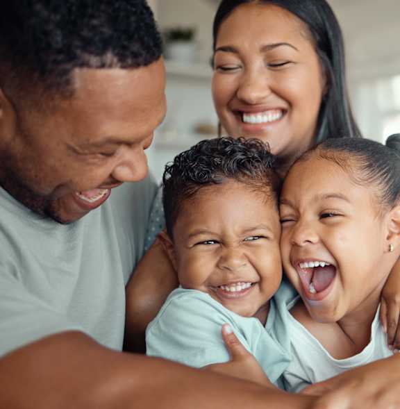 A family of four is hugging and smiling together.