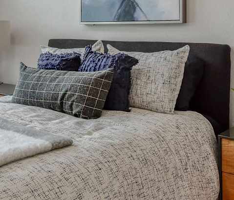 A bed with a white comforter and pillows with a blue and grey pattern.