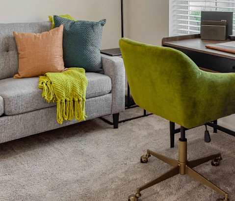 A green chair sits next to a grey couch with a yellow throw.