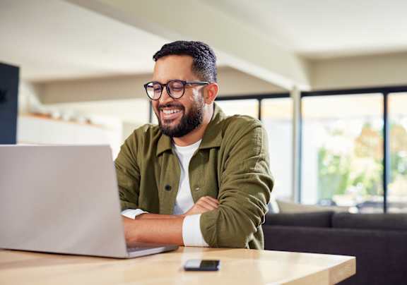 A man with glasses and a green jacket is smiling while using a laptop at Walker Place Apartments, Texas, 76643