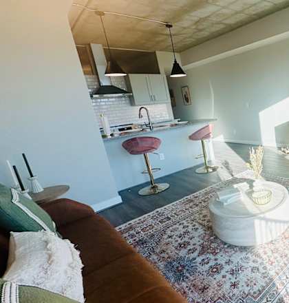 A living room with a rug, a couch, a television, and a kitchen area in the background.