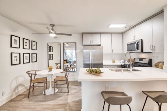 an open kitchen and dining area with a white table and chairs and a white counter at The Meadows Apartments, Culver City , CA 90230