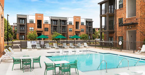A swimming pool surrounded by chairs and tables in front of apartment buildings.