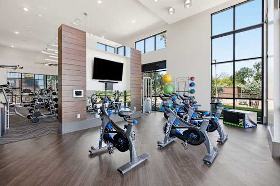 A gym with a row of stationary bikes and a television.
