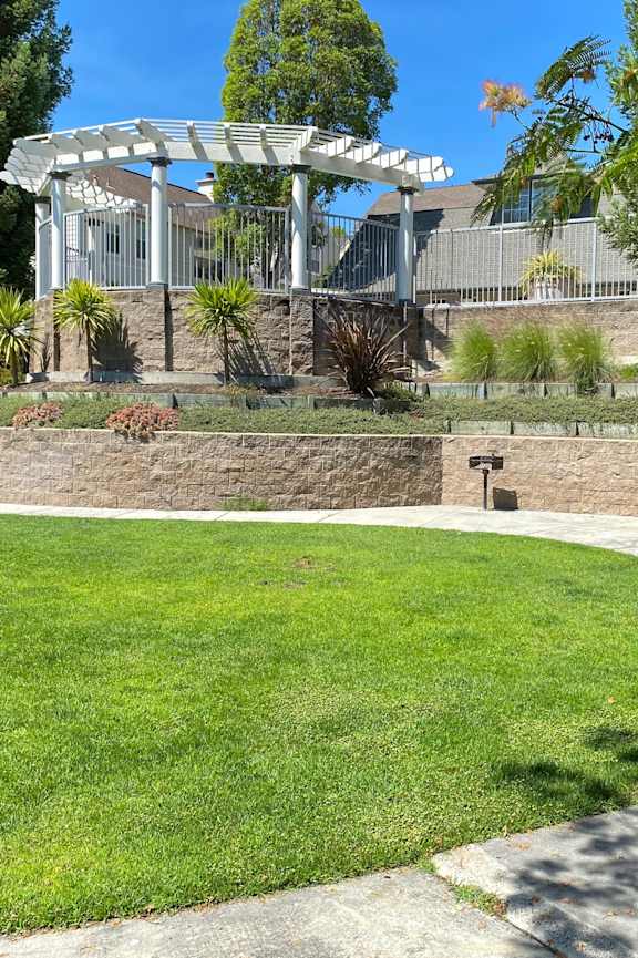 A white pergola is situated in a grassy area. at Westmont Place Townhomes Apartments, Santa Cruz, 95060