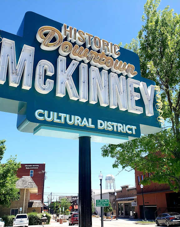 A sign for the Historic Downtown McKinney Cultural District stands in front of a tree.