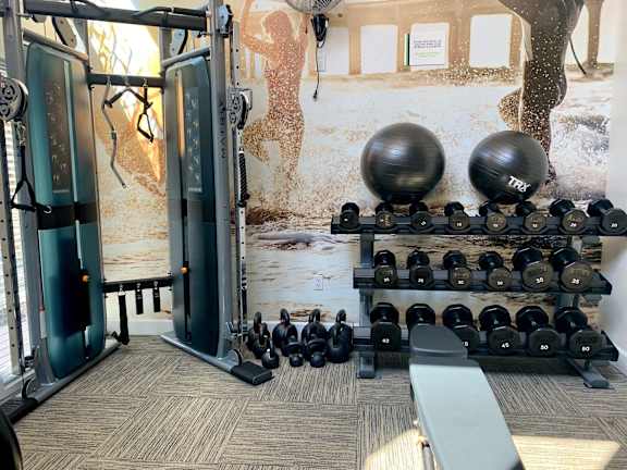 A gym with a variety of equipment including dumbbells, weight plates, and a bench.at Pacific Bay Club Apartments, San Diego, CA 92117
