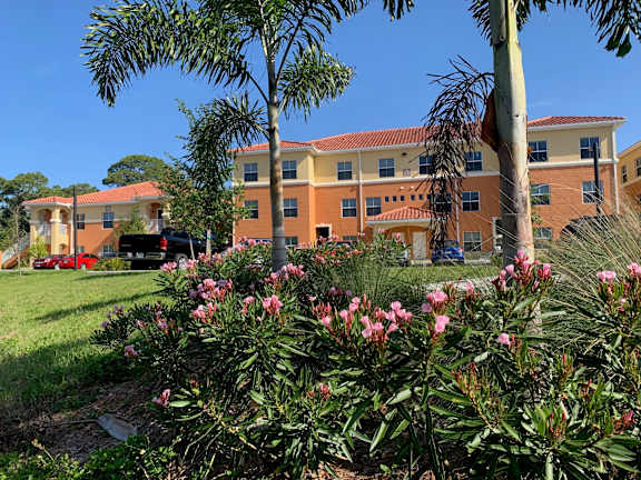 A building with orange walls and a red roof is surrounded by greenery and trees.