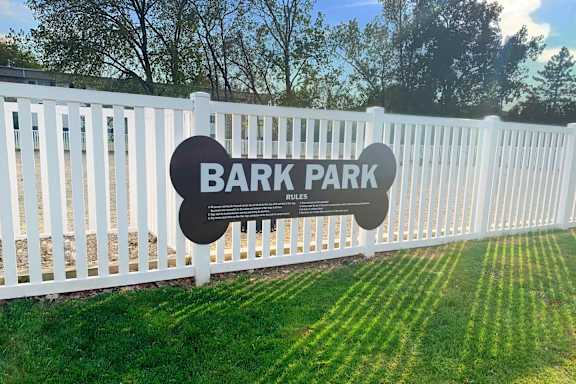 A sign that says Bark Park rules stands in front of a white fence.
