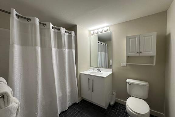 A white bathroom with a toilet, sink, and shower curtain.at 66 Main, Yonkers, NY 10701