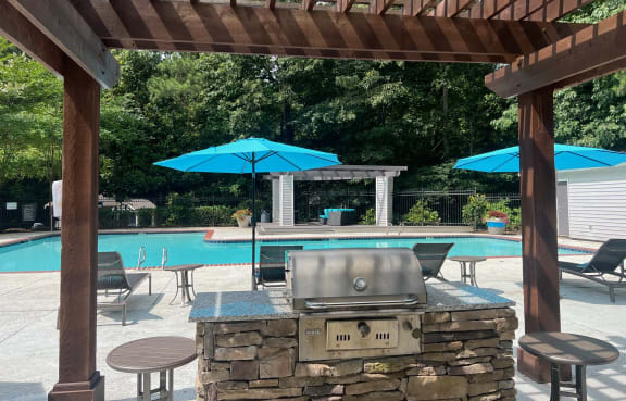 a pergola with a grill and umbrellas overlooking a swimming pool