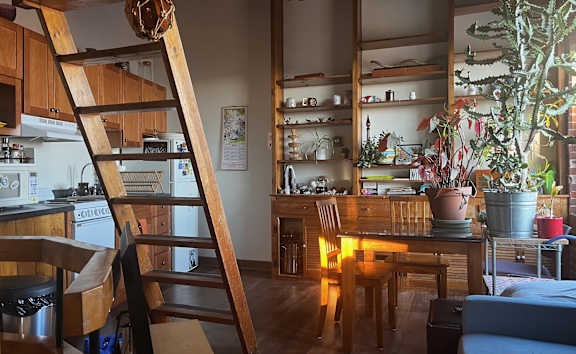 A wooden ladder is leaning against a wall in a room with wooden floors and furniture.